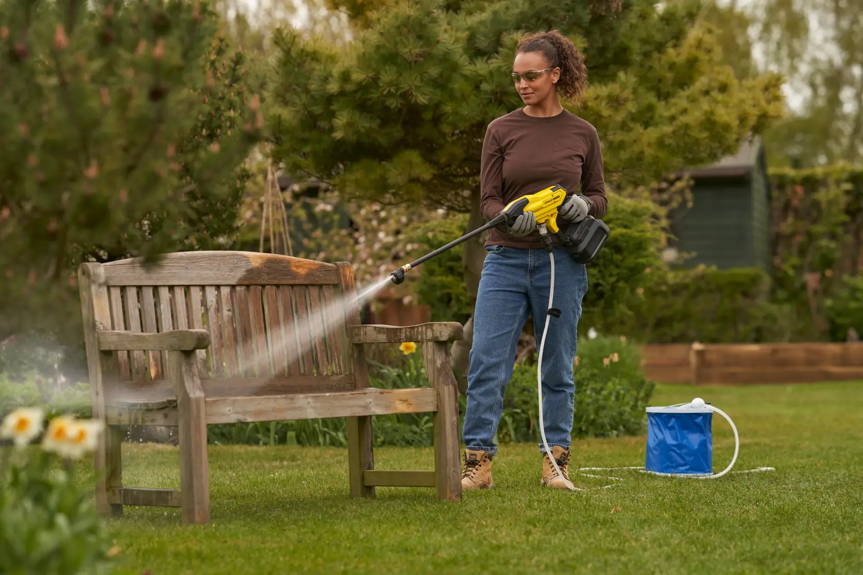 STANLEY SFMCPC93M1 pressure washer in use cleaning a wooden bench outdoors, garden setting.