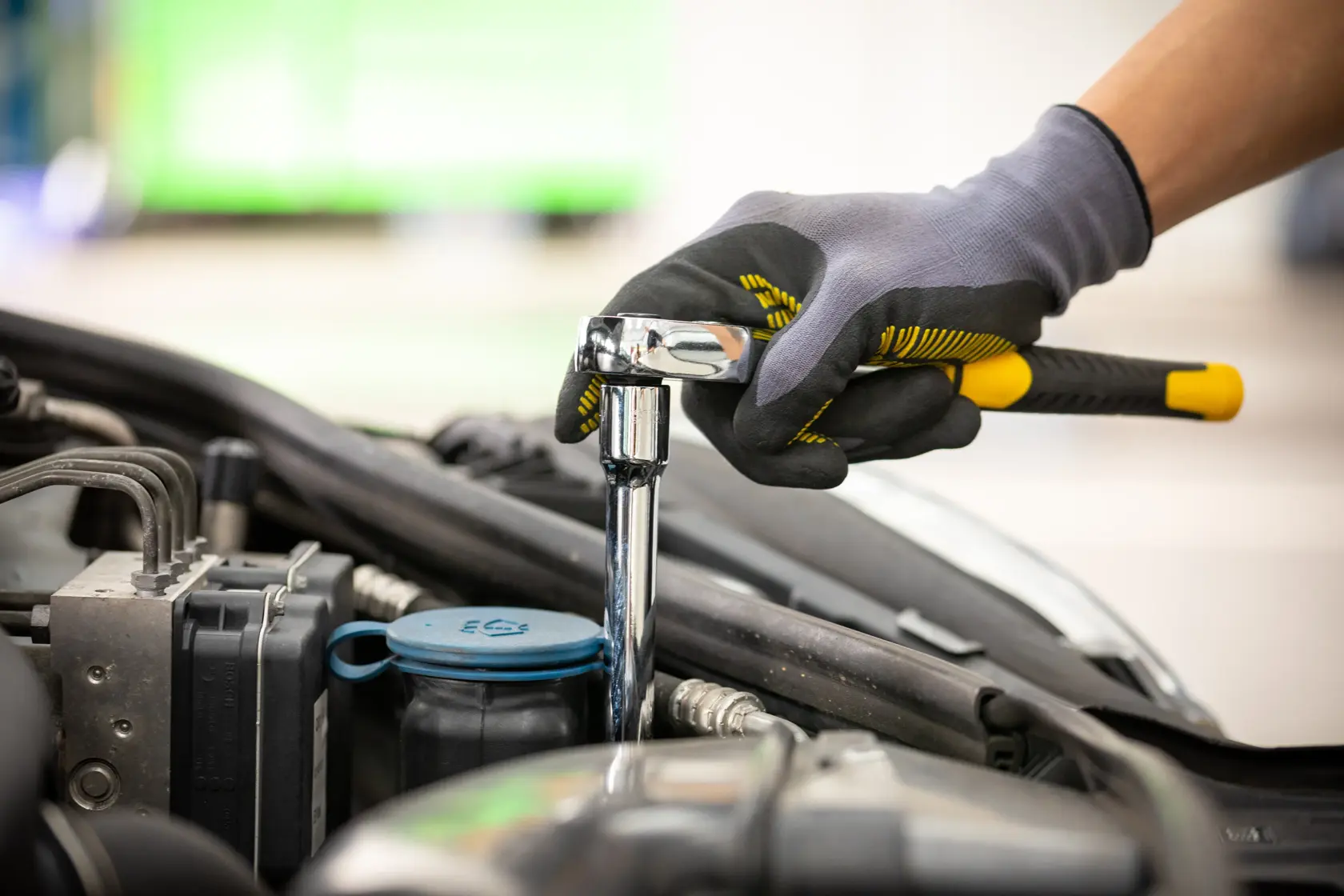 STANLEY STMT86407-0 ratchet wrench in use by gloved hand tightening bolt on car engine, side angle.