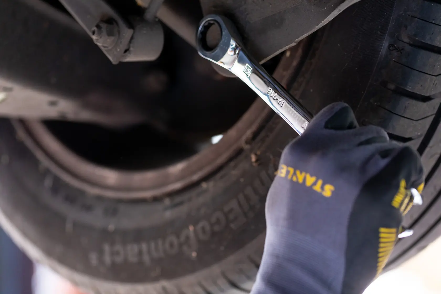 Stanley STMT89912-0 ratcheting wrench used on a car wheel, hand in Stanley glove visible.