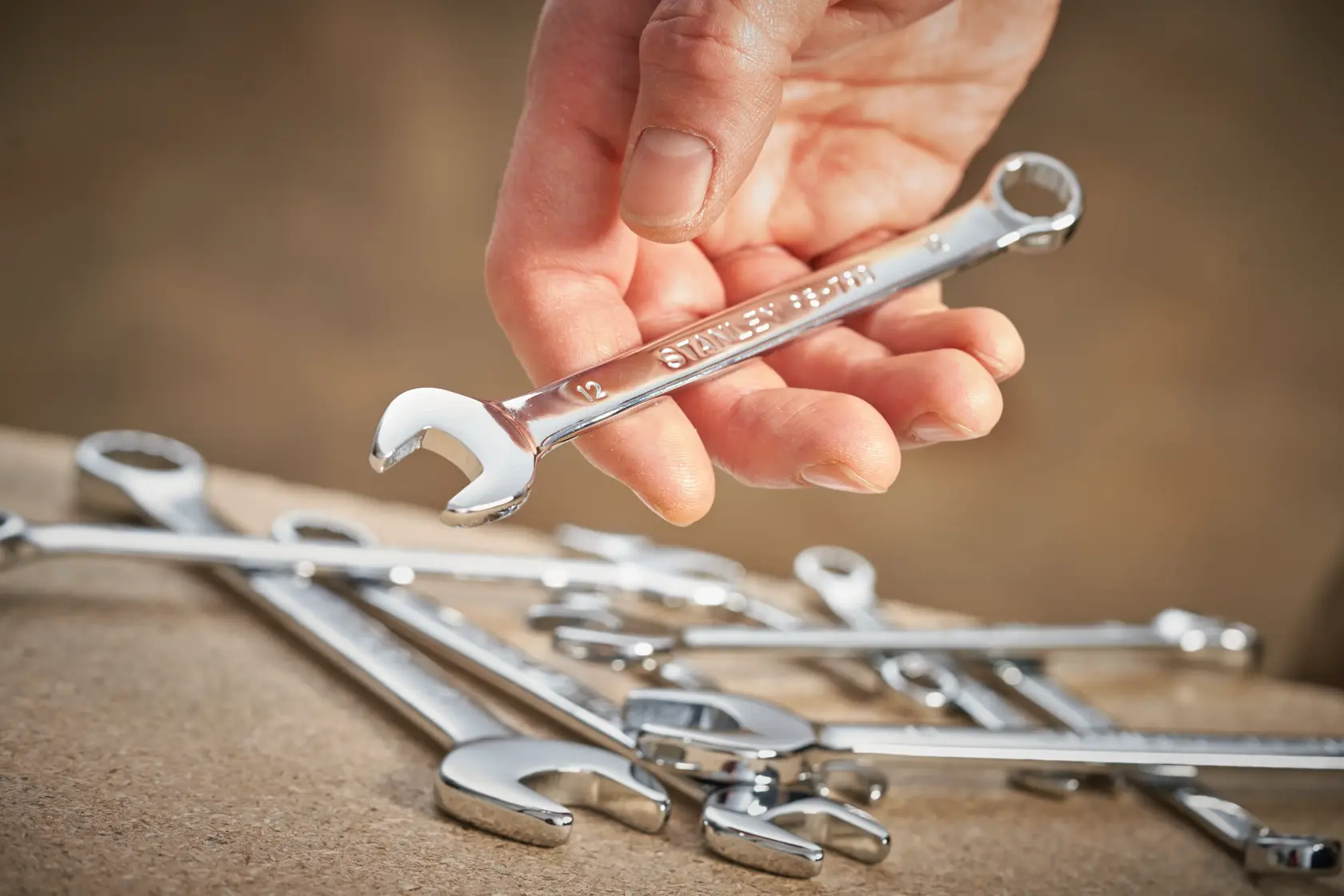 STANLEY STMT95908-0 chrome combination wrench held by hand, with other wrenches on a work surface.