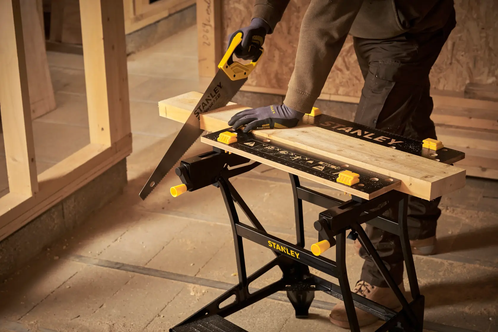 STANLEY STST83400-1 portable workbench with wood clamped, handsaw cutting wood, workshop setting.